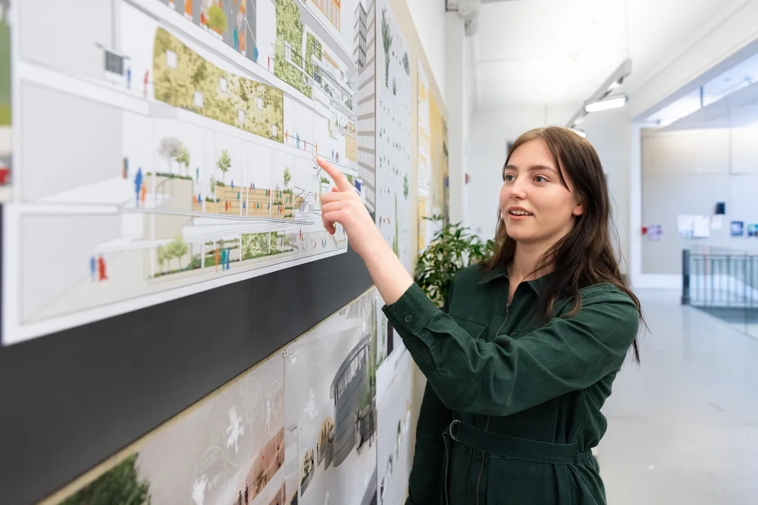 Architecture student points to renderings presented on presentation wall.