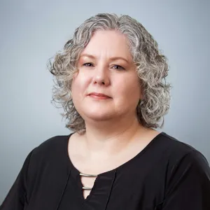 Cherri Wells smiling in front of a grey background.