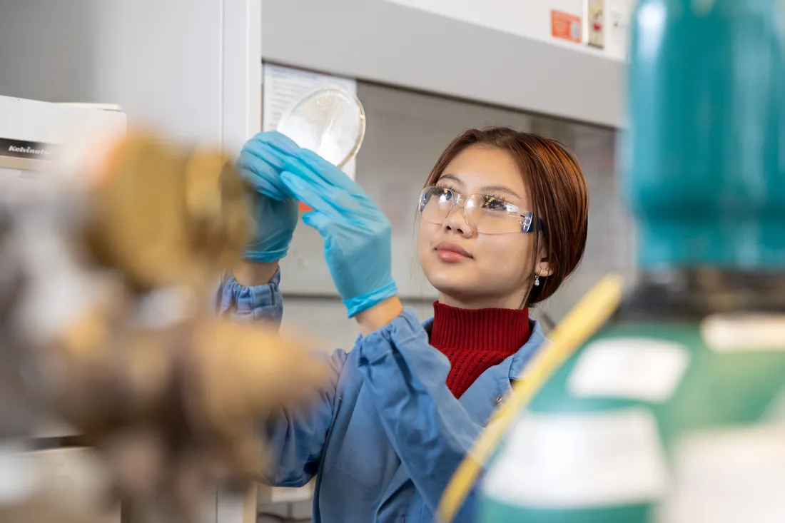 person in lab coat and safety glasses in a laboratory