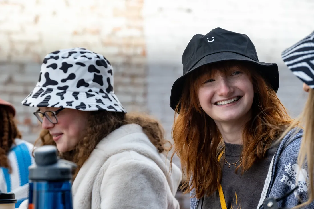 Two students wear hats and smile together.