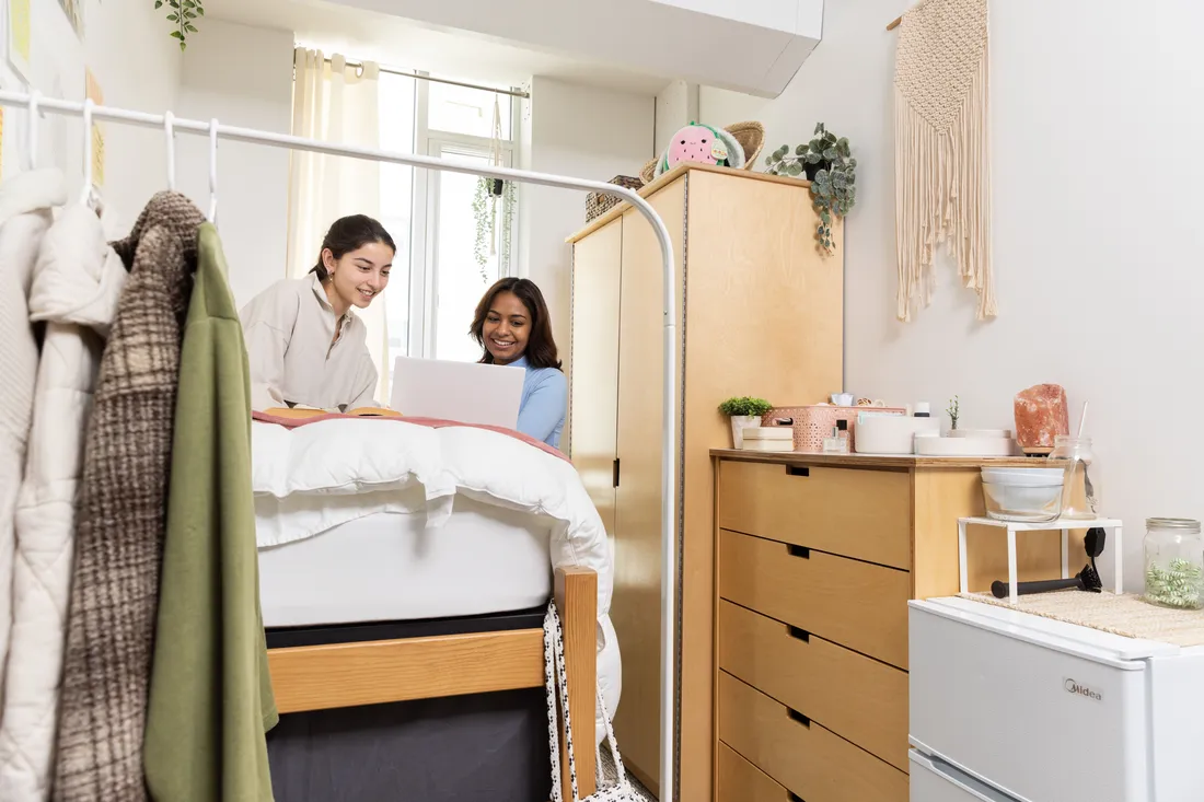 Two students looking at a computer in dorm room.