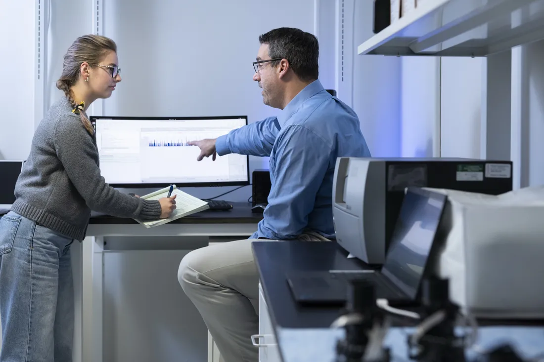 Person showing information on computer while another person takes notes.