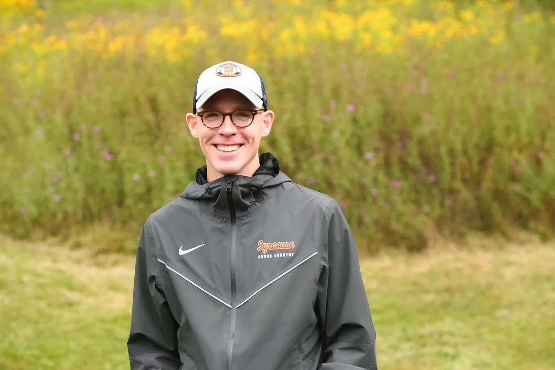 Coach smiling at a camera in a field.
