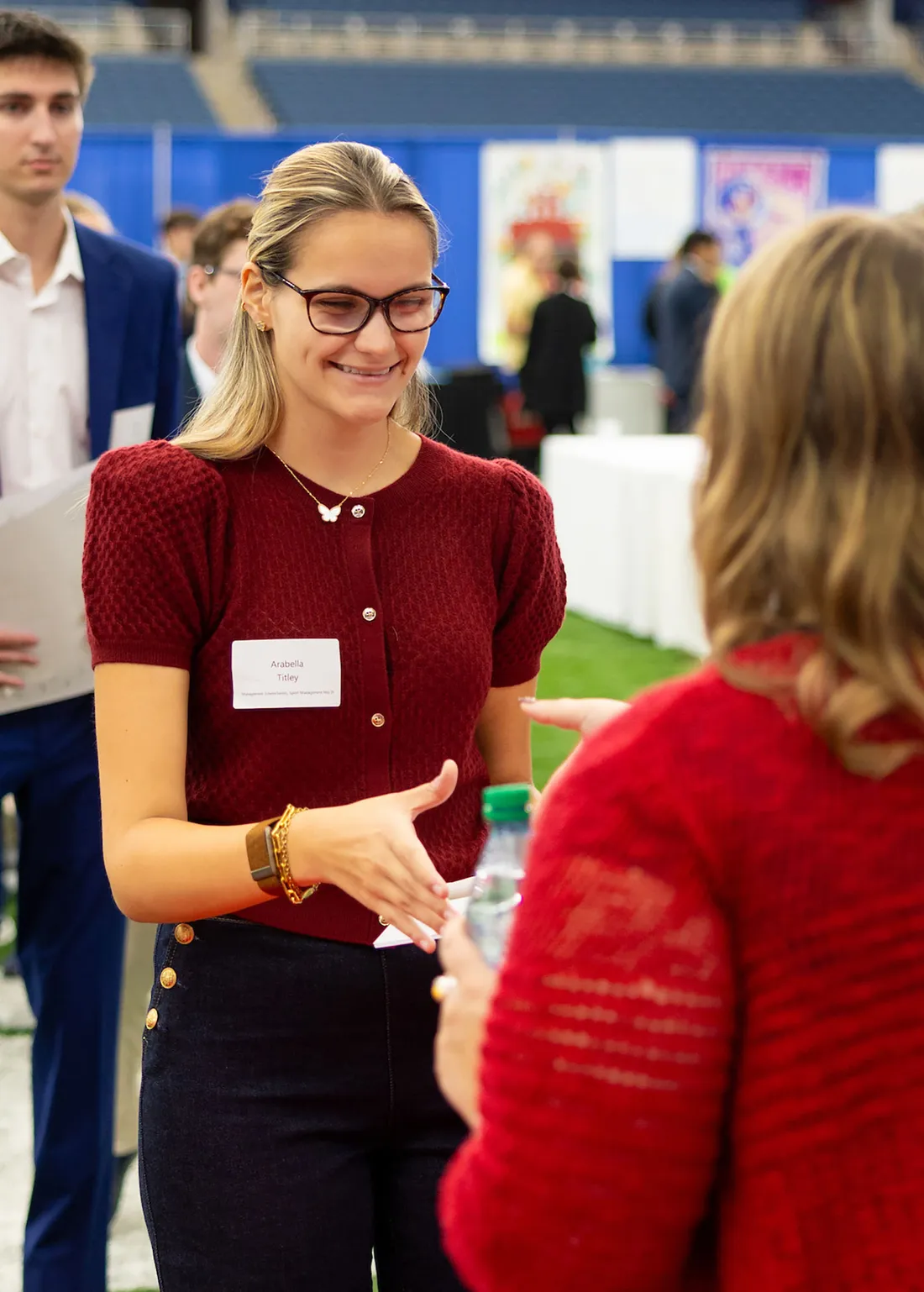 A young woman in a red sweater shaking a recruiters hand.