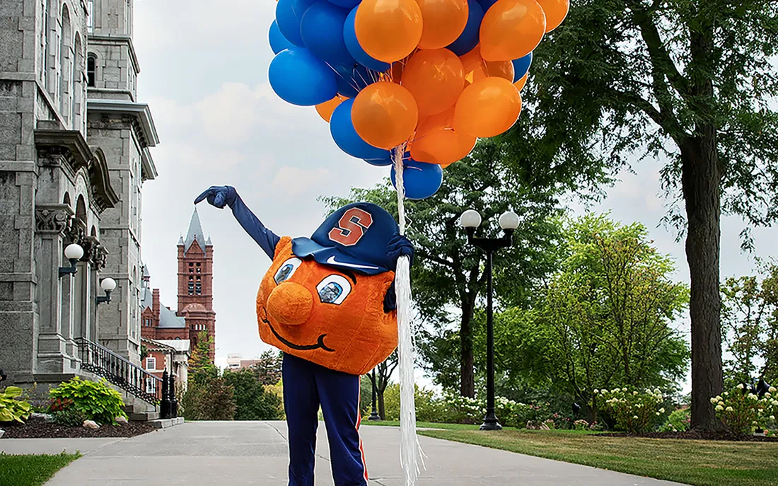 Otto the orange holding balloons.