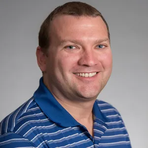 Jason Scharf smiling in a blue and white striped polo.