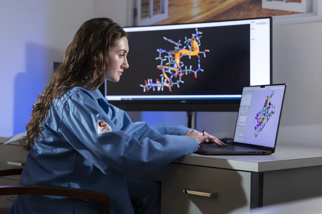 Person sitting at desk looking at 3D models of molecular structures on computer.