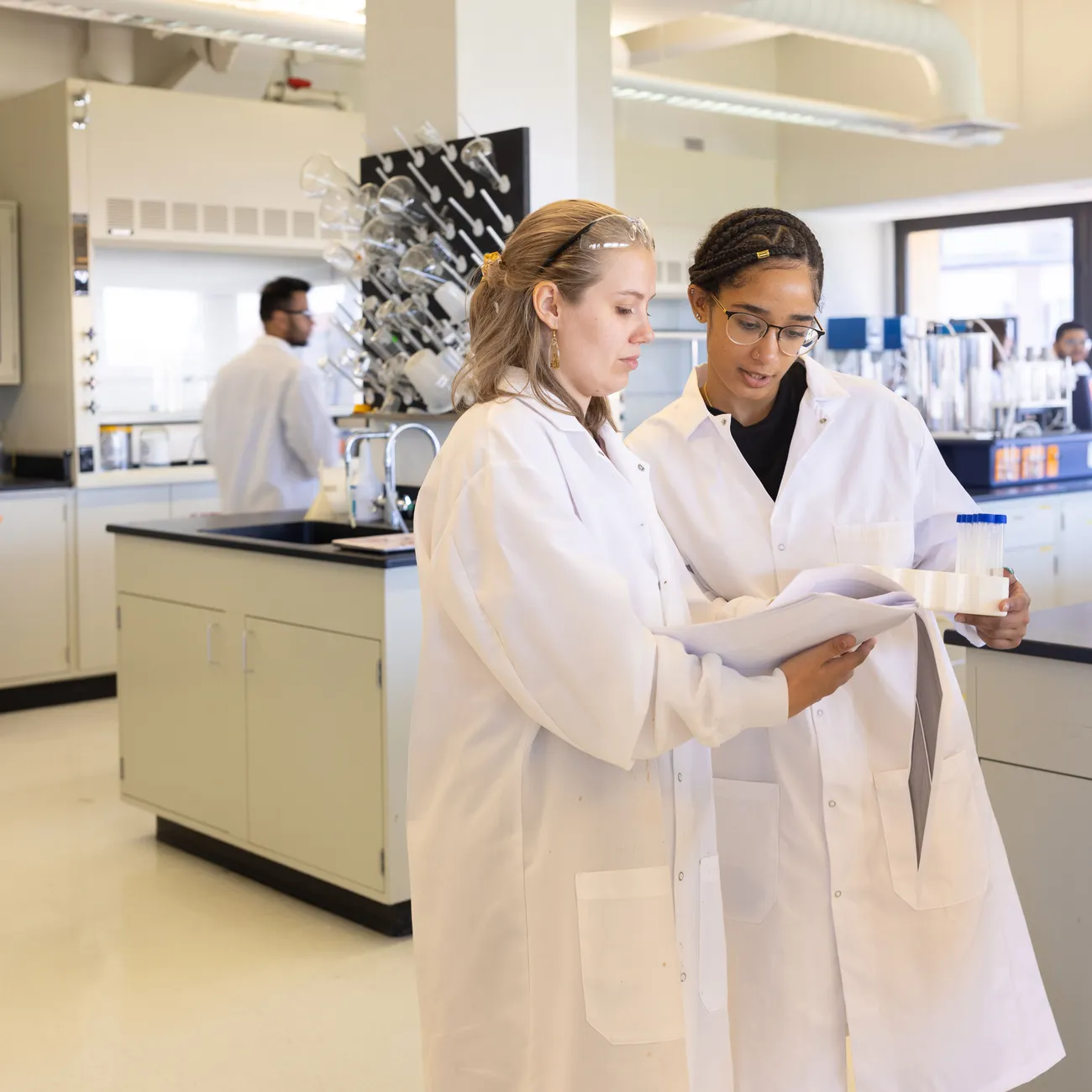 students in white lab coat review documentation inside a laboratory.