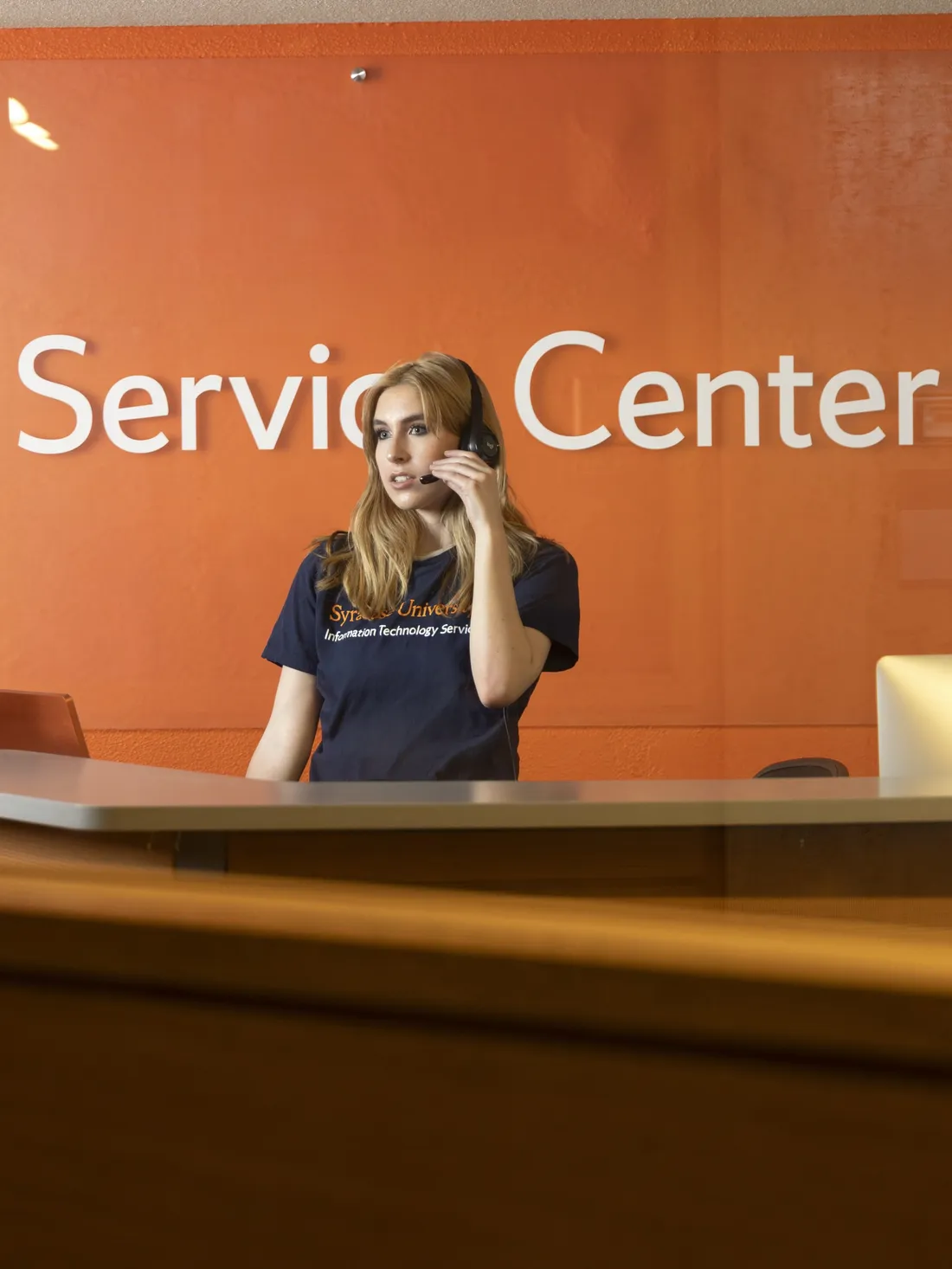 Ruby Dainesi '27 standing at the Information Technology Services desk speaking through a headset.
