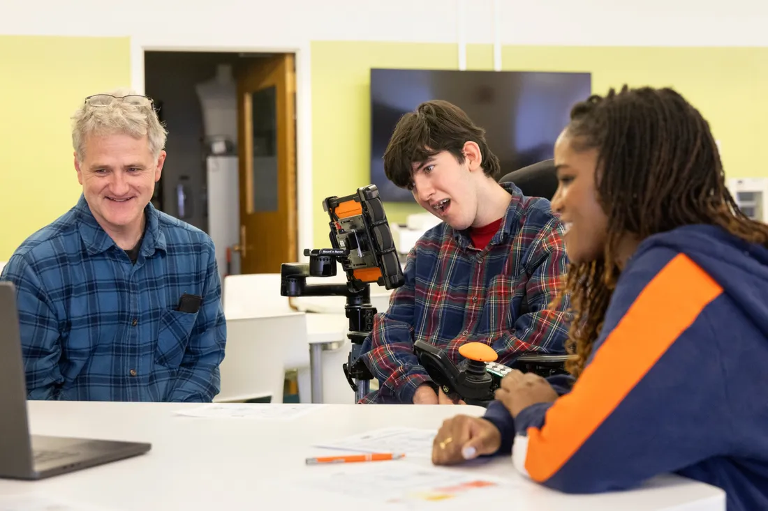 Syracuse University student Samara Tomlinson sitting at a table with high school student Leo True-Frost and his father.