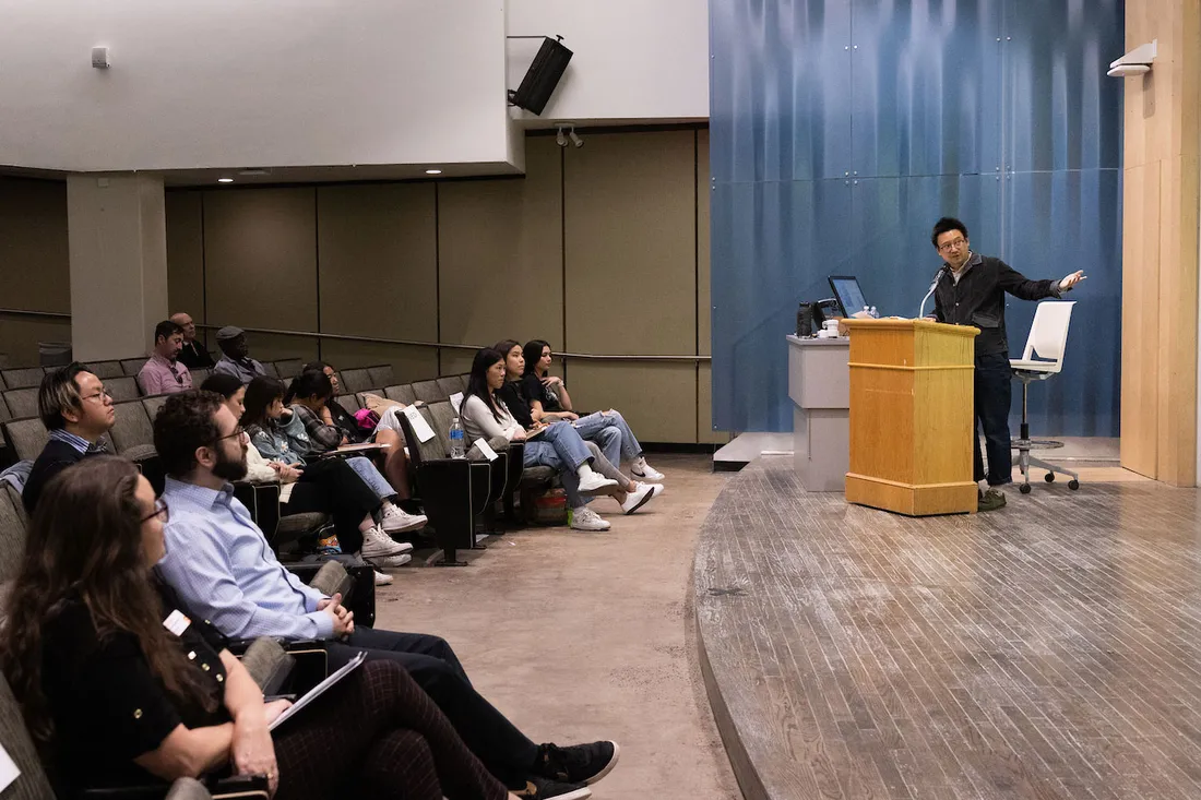 Hua Hsu stands at lectern in front of room of onlookers giving a lecture.