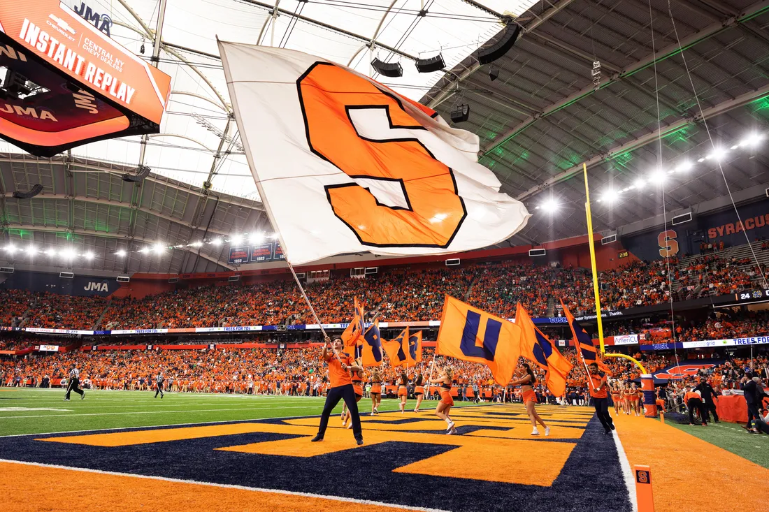 Wide shot of the Syracuse University flag being waived by a student on game day in the JMA Wireless Dome.