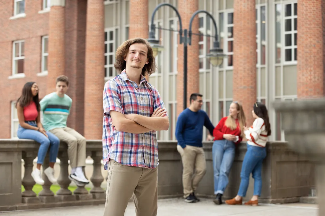Student stands and smiles with arms crossed.