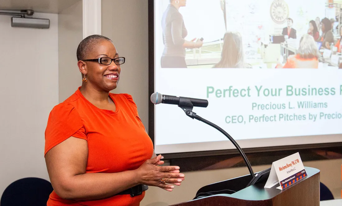 Mariama Boney speaking at a podium with a presentation on the screen behind her.