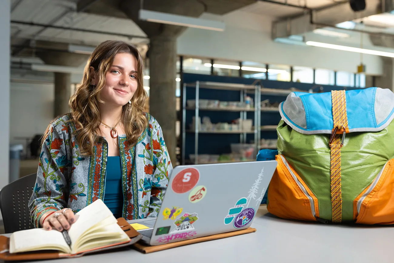 Student smiling at camera while working on a laptop.