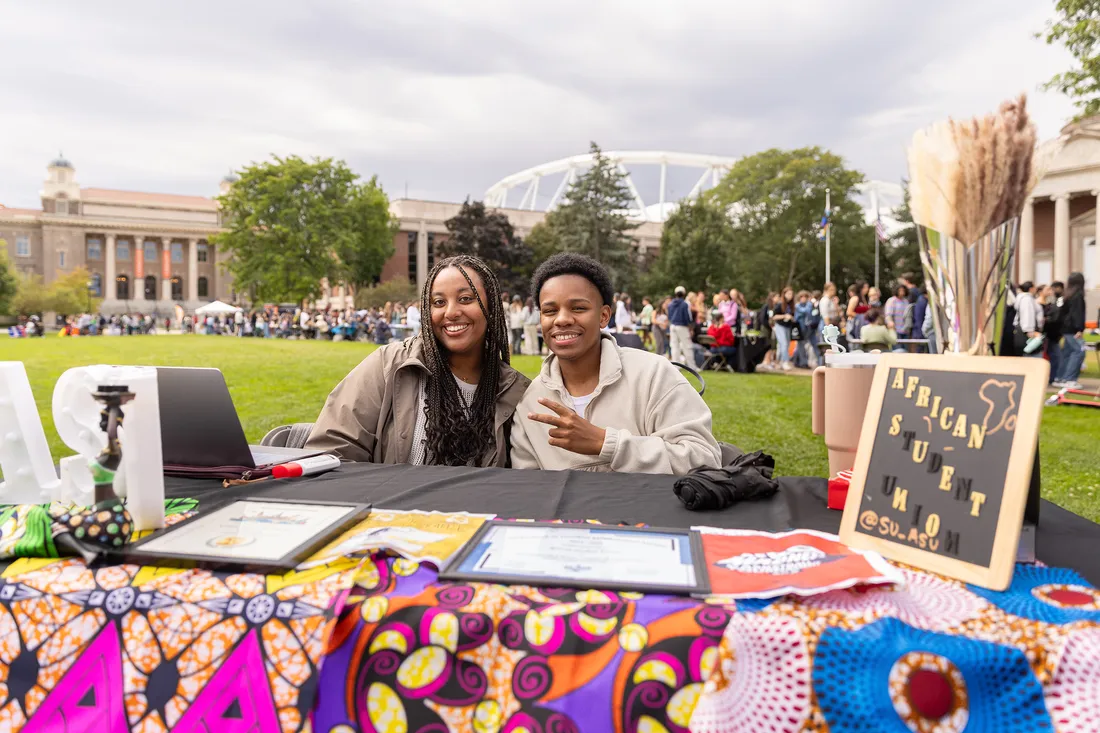 Two students sitting at a table at the clubs and organizations involvement fair.