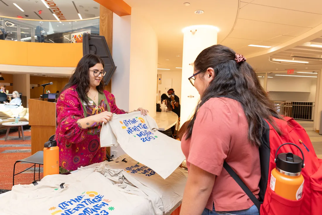 Students look at Latine Heritage Month tee shirts on a table in Schine Student Center.