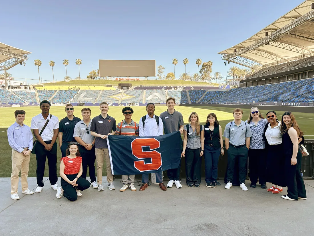 Students on an immersion trip to Los Angeles standing in the LA Galaxy stadium holding a Syracuse University flag.