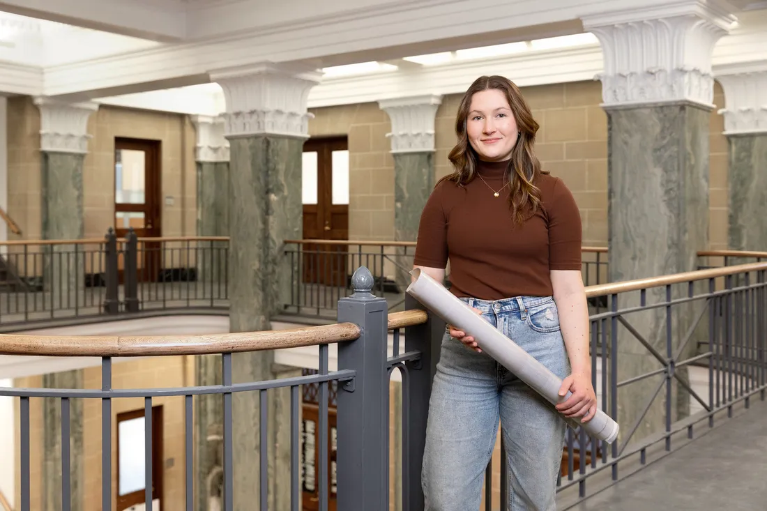 Marykate Kregg holds blueprints rolled up, posing for camera.