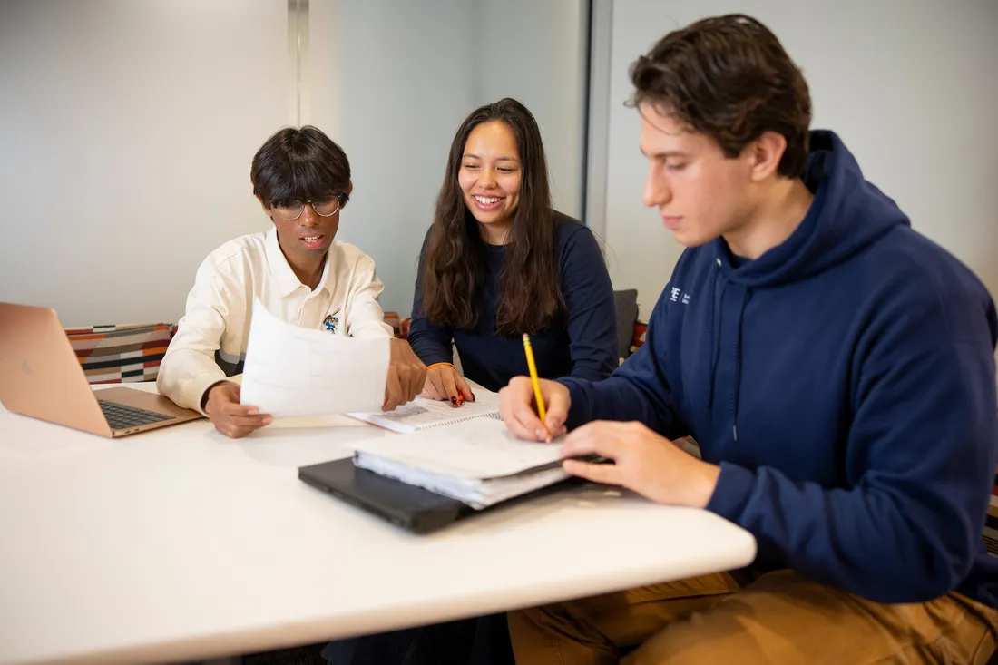 Two students sitting with a professor in the campos student center.