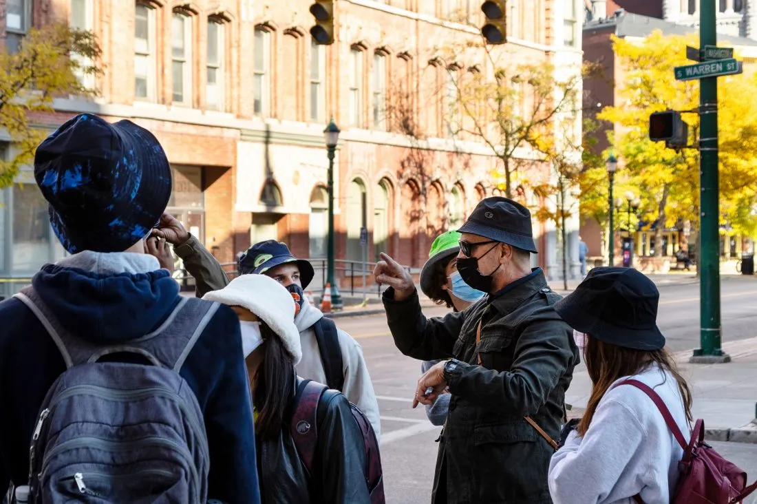 Person speaking to a group of young adults on the street in the city of Syracuse.