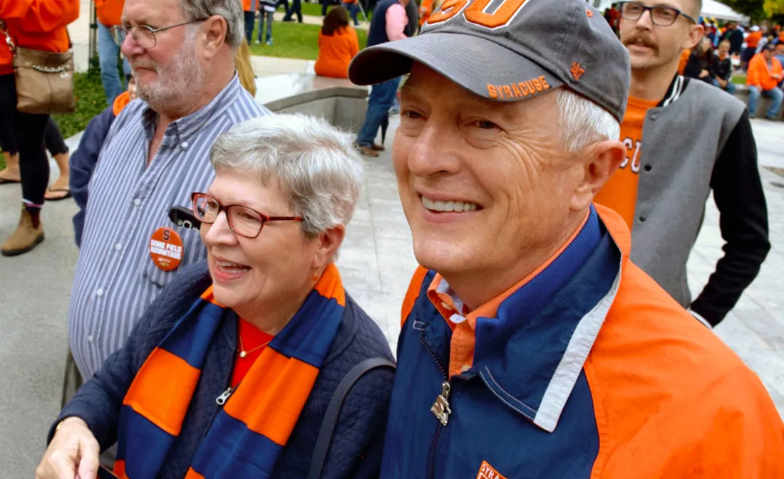 People smiling at football game with their SU branded gear on..