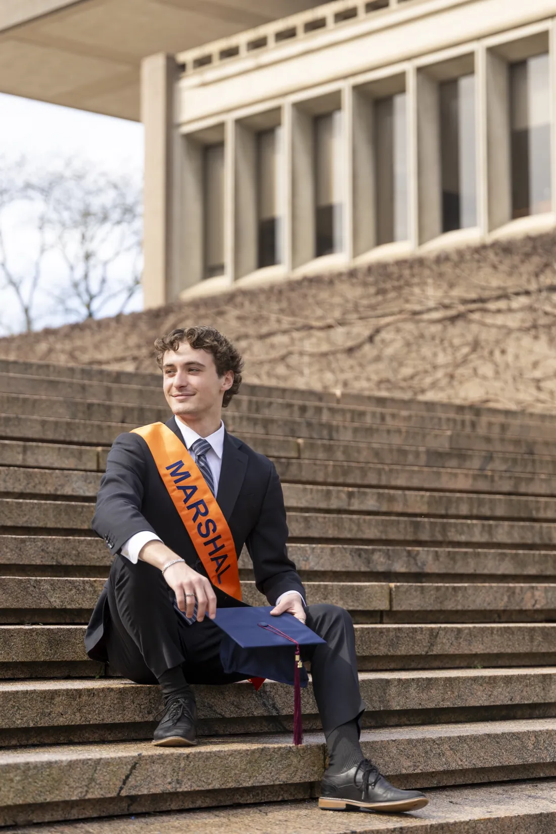 Steven Labovitch '26 sitting outside on a staircase wearing his Student Marshal sash.
