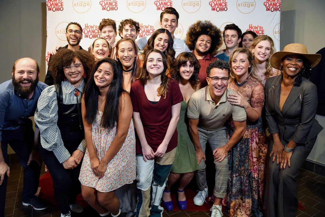 Group photo of smiling actors in front of a backdrop that says "Syracuse Stage, How to Dance in Ohio."