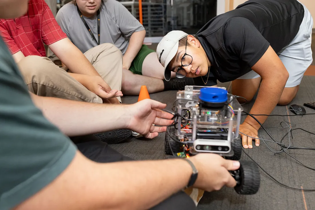 Students on the floor observe the motion of a robotic AI car.