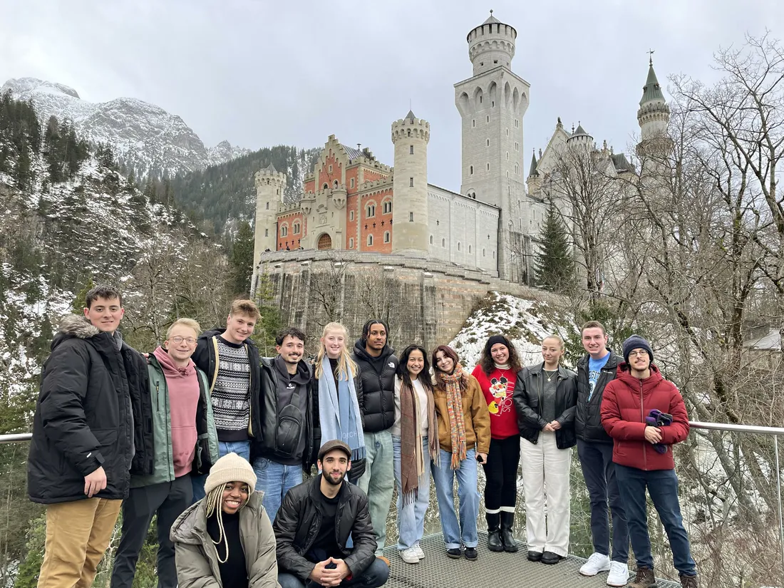 Students standing in front of a scenic castle in the mountains