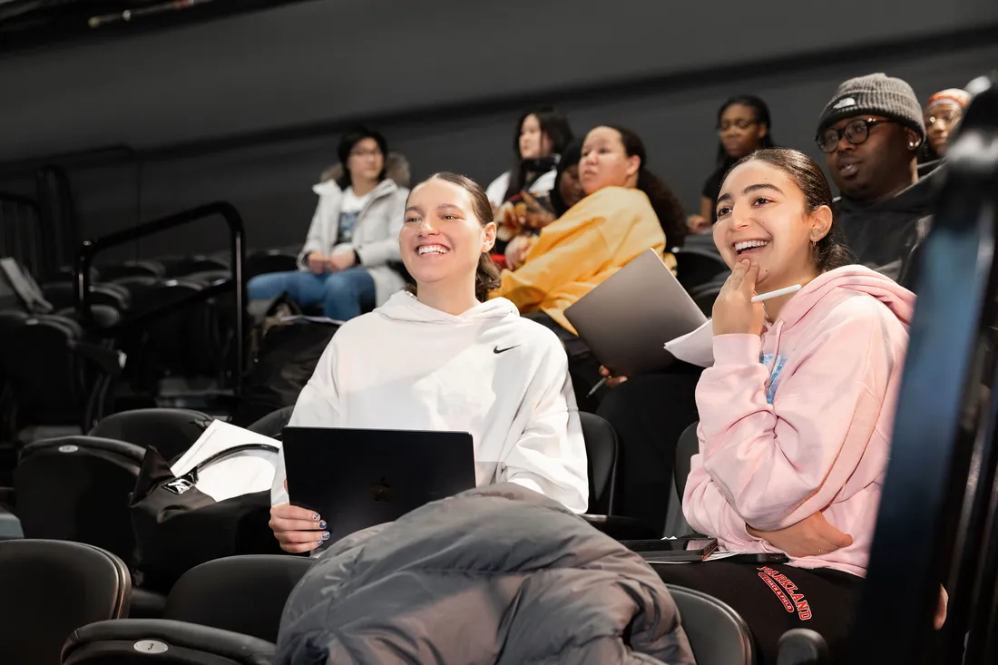 Two students sitting and smiling in Professor Tanisha Jackson's classroom.