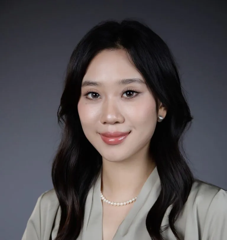 Leah Li smiling in a grey button up top with a pearl necklace on.