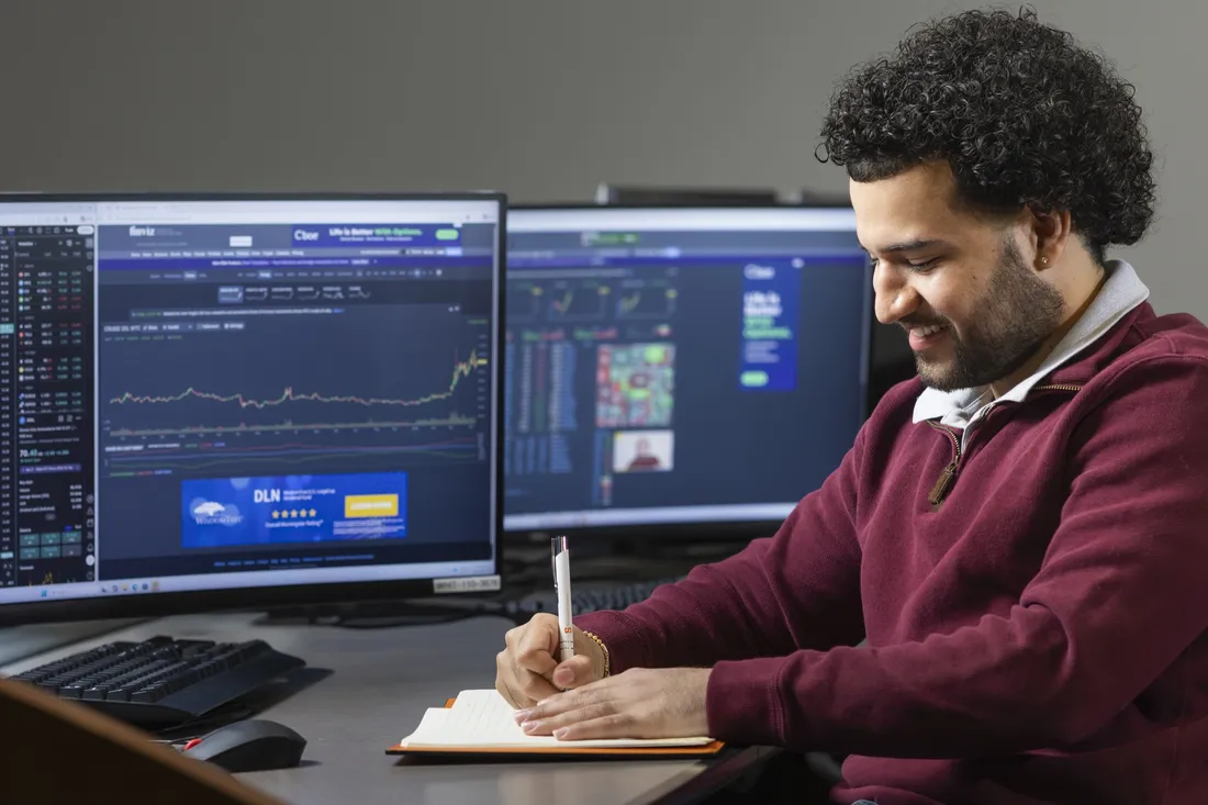 Thomas Castro-Chalarca '26 sitting at a desk in the Whitman Atrium and writing in a notebook.