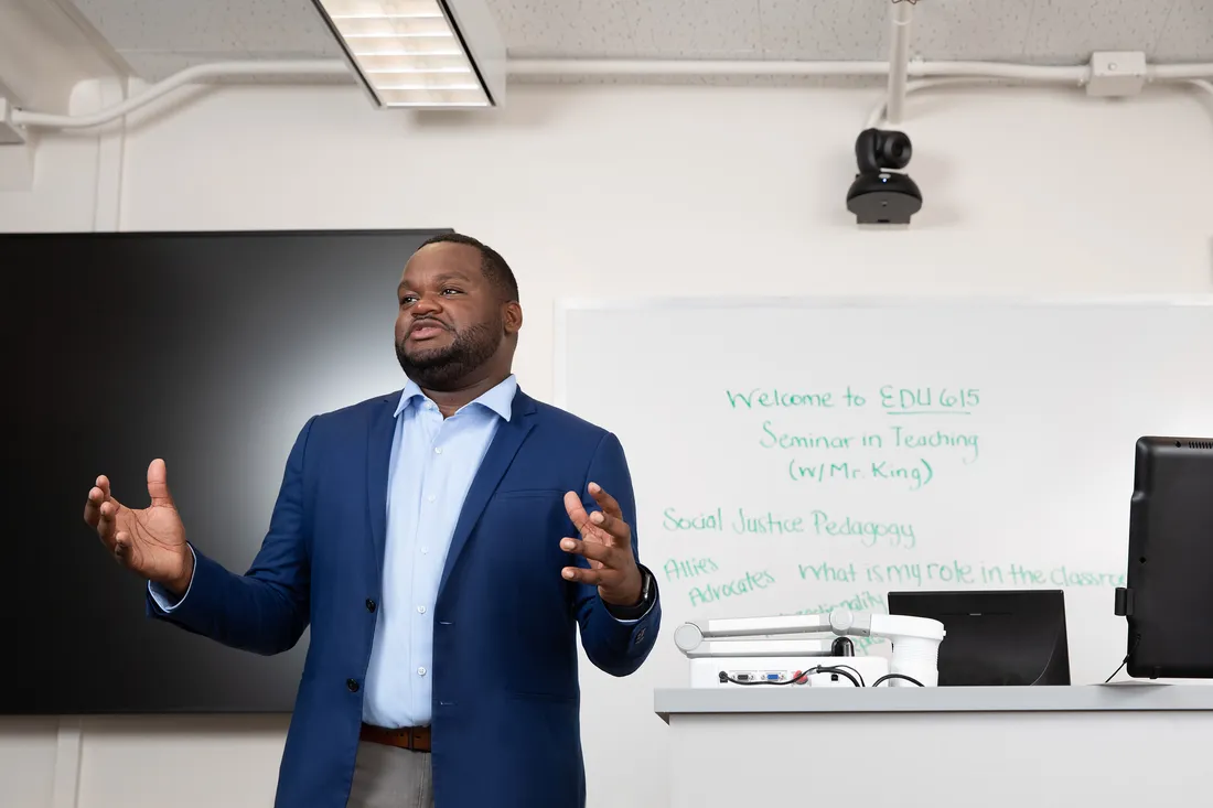 Graduate student Terrance King teaching in front of class, expressing with his hands in the air.