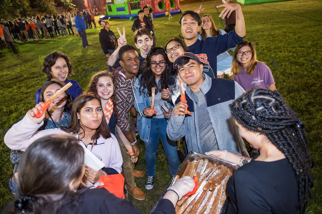 Group of students poses for a photo on a sports field holding churros