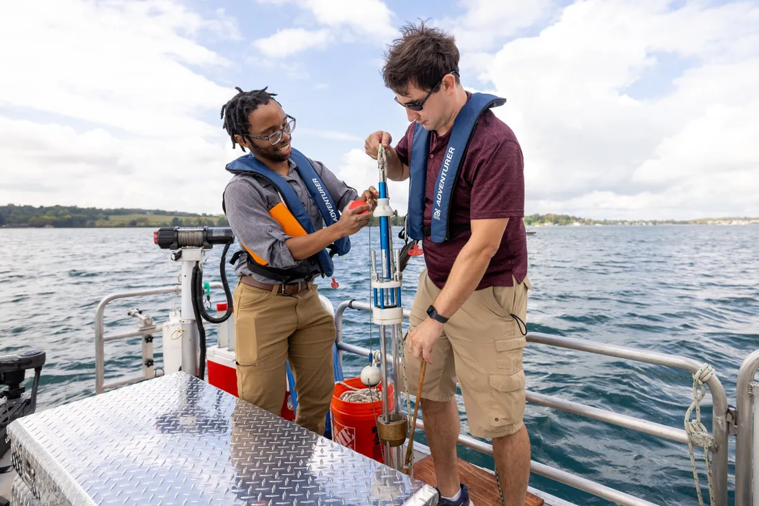Two students hold a piece of sonar technology on a dock at Skaneateles Lake.
