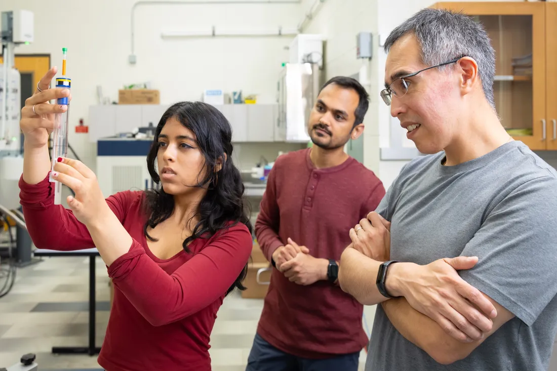 Professor Carlos Castañeda looking at a testing tube in a lab alongside two of his students.