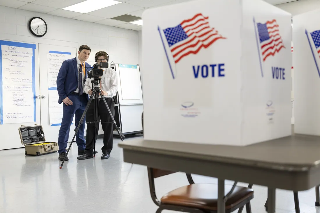 Two people standing behind video camera at an election polling place.