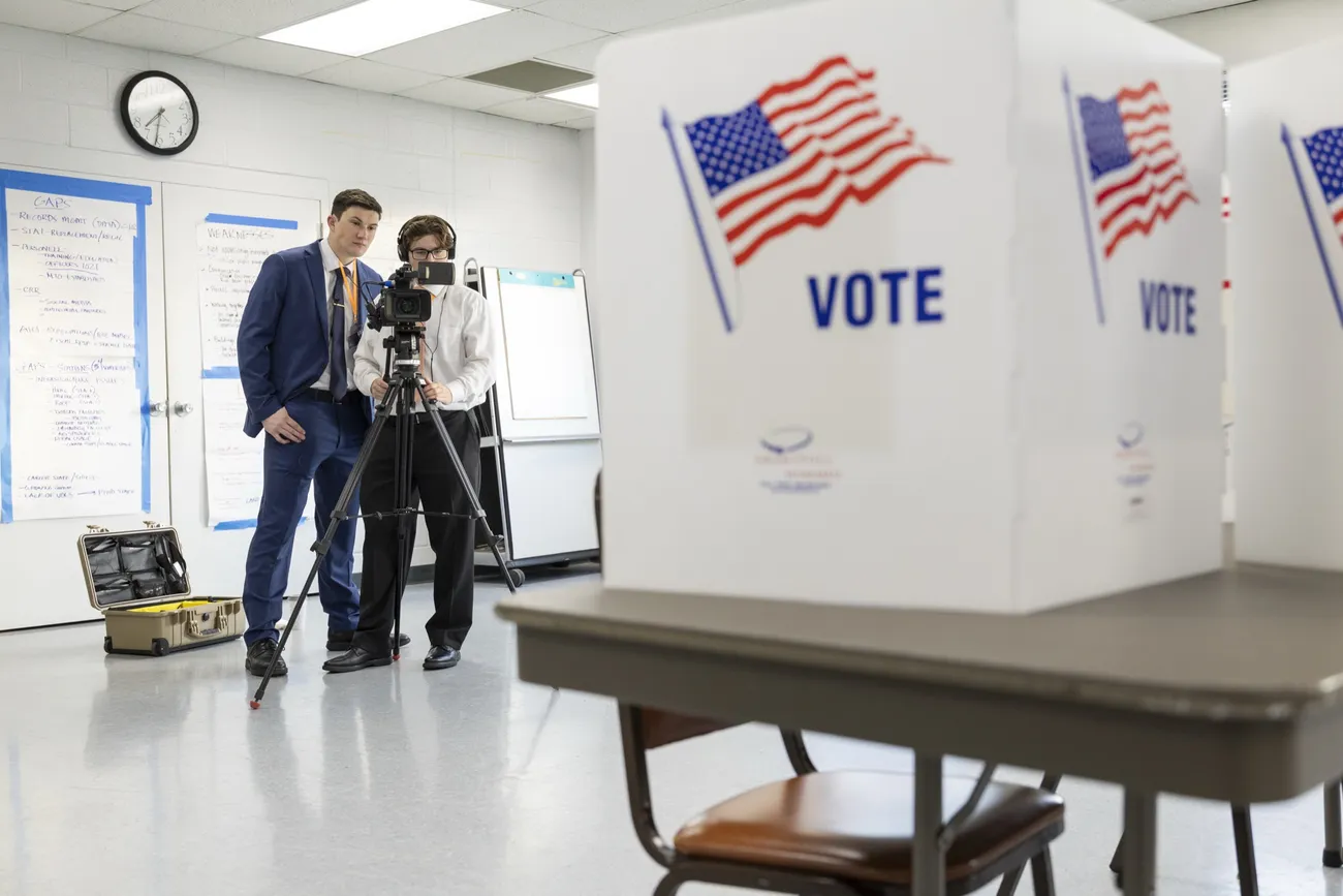 Two people standing behind video camera at an election polling place.