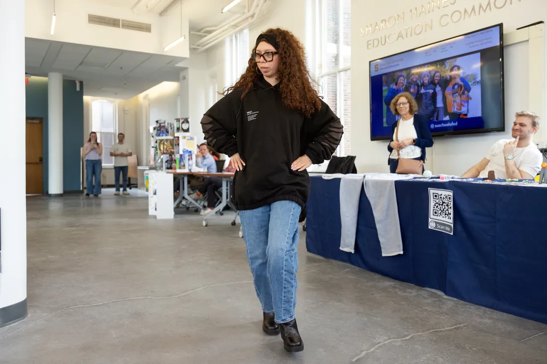 Student Sasha Soraci standing and modeling a sweatshirt from the inclusive clothing brand SOLACE Collective.