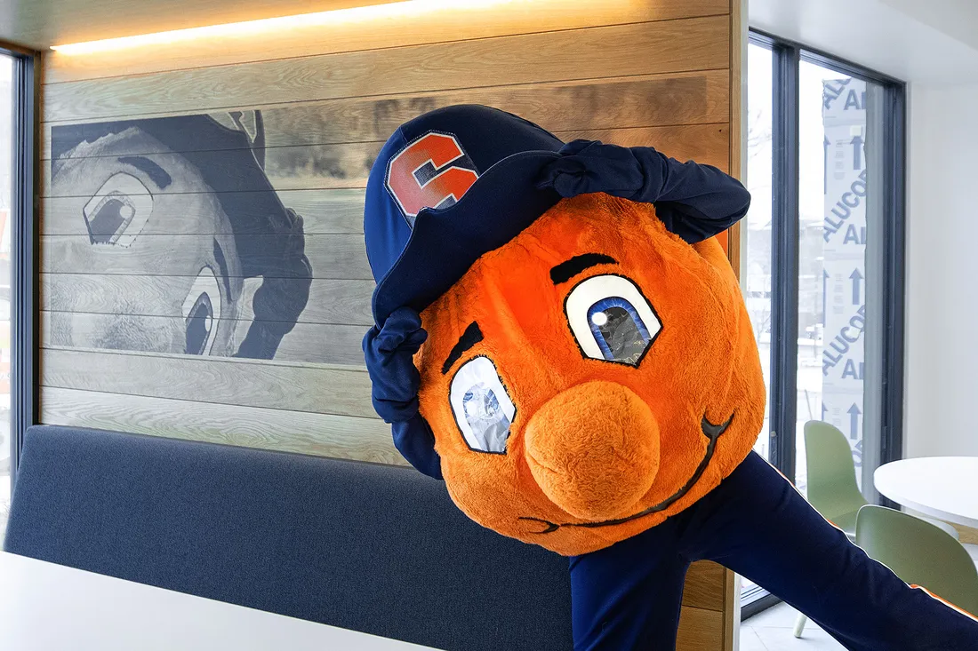 Otto the orange mascot standing with a picture of itself.