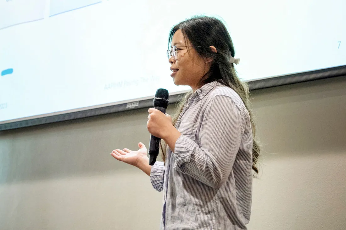 Sharon Lee holds a microphone in front of presentation speaking to room.