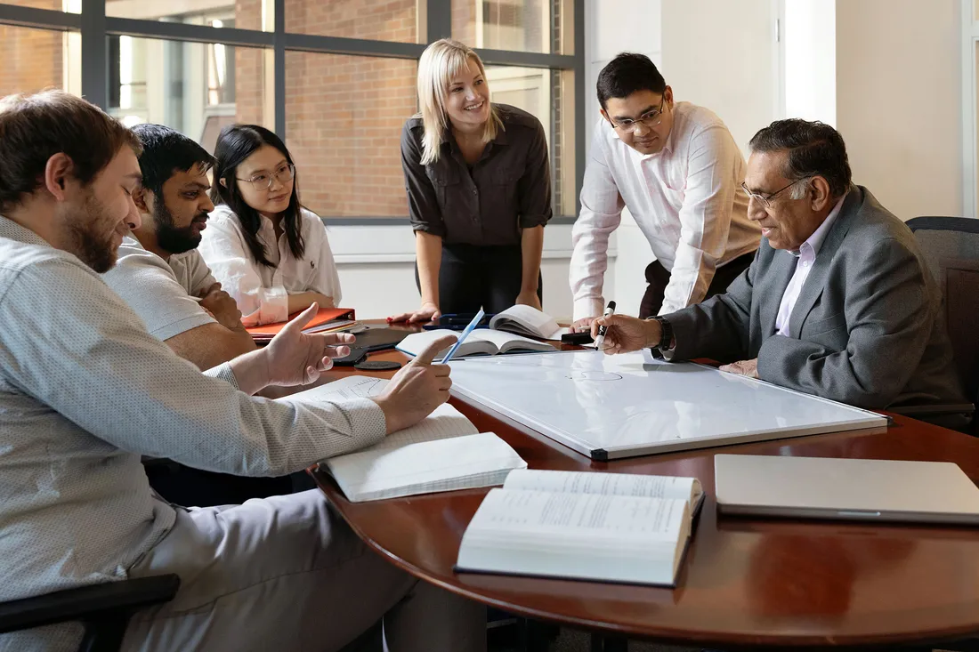 Professor and students sitting at table working together.