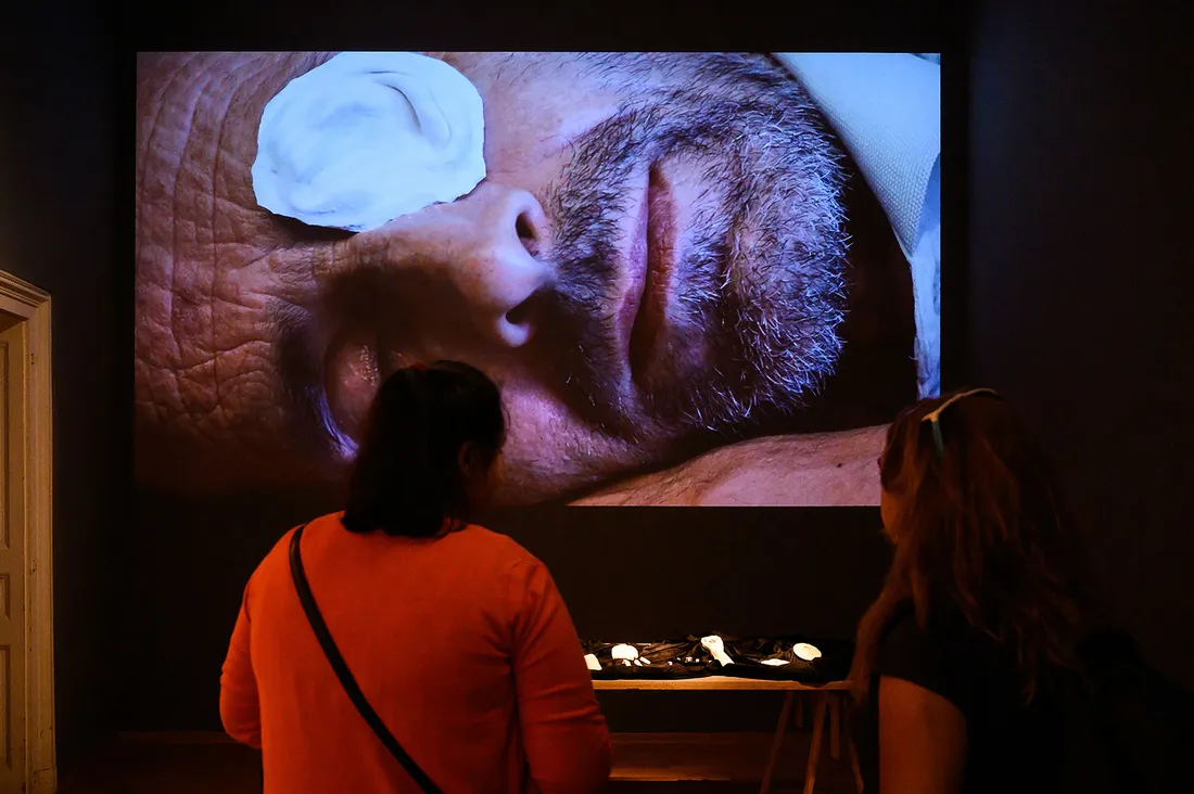 Onlooker stands close to screen on which is projected the face of a man wearing a plaster eye patch.
