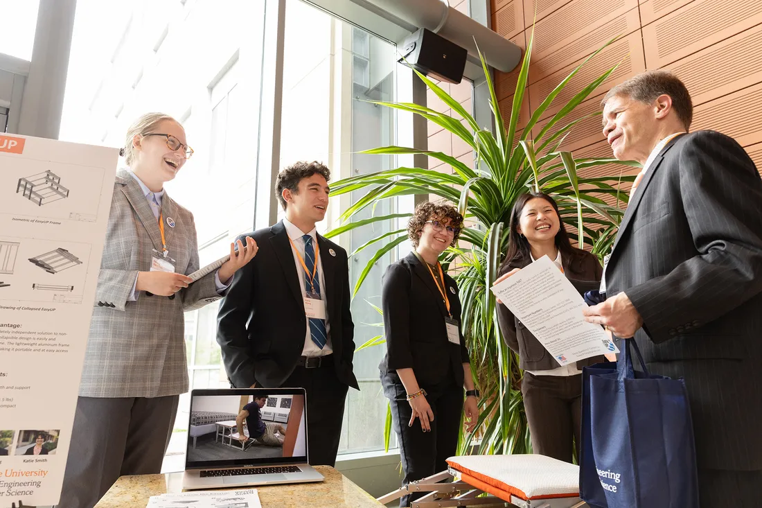 Students in business clothes speak to presentor at invention presentation.