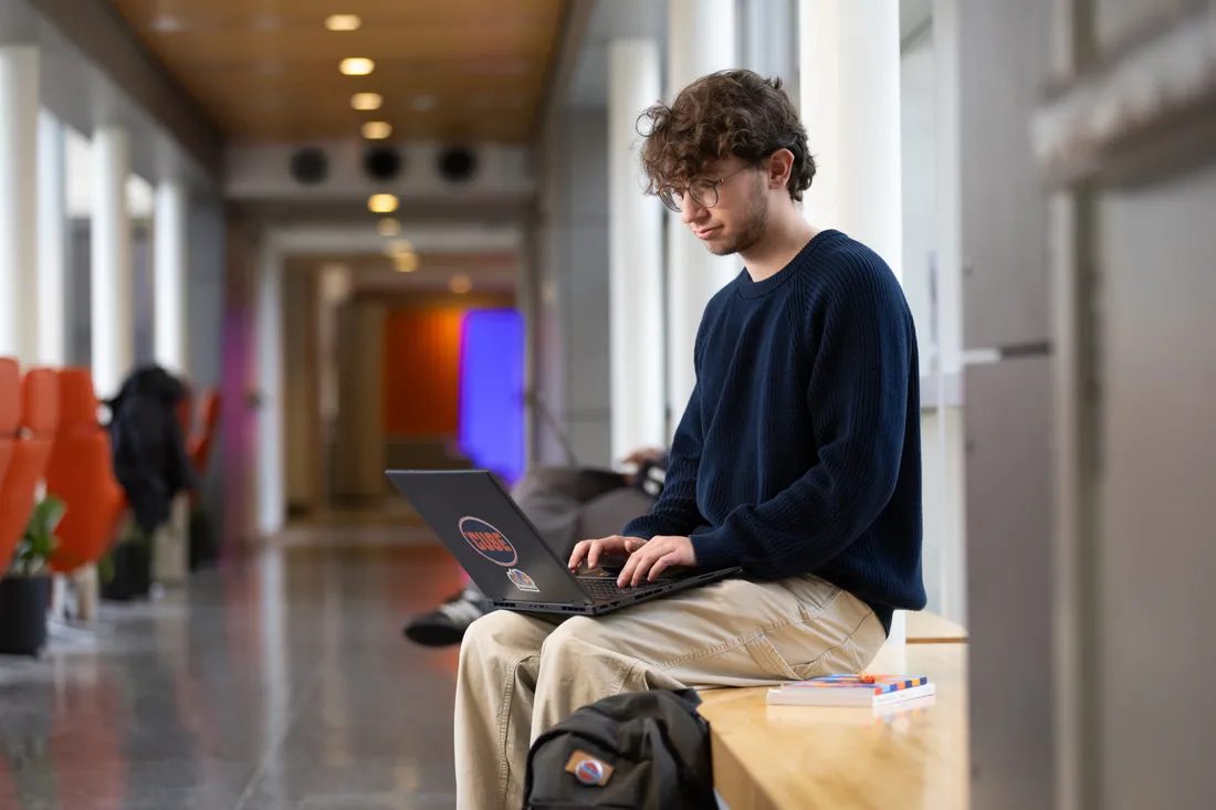 Person sitting on bench typing on laptop.
