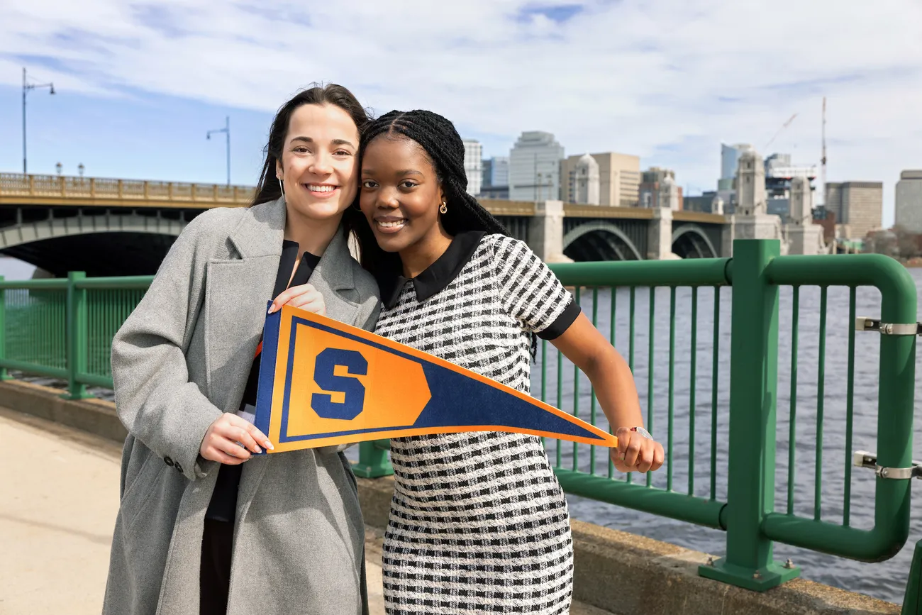 Two people walking on a sidewalk in Boston while holding a Syracuse University flag.
