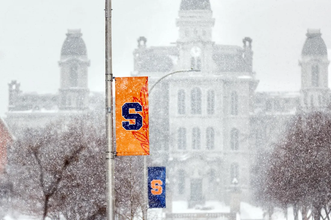 Syracuse University flags on a snowy campus in front of the Hall of Languages.