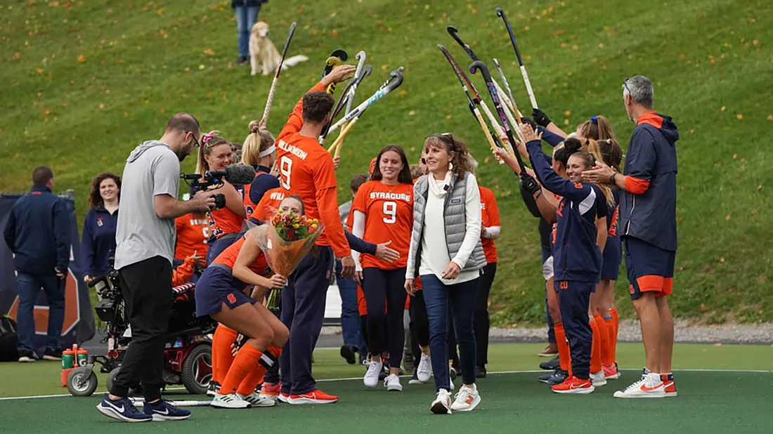 Landscape photo of Sullivan walking through a tunnel made by other athletes and their field hockey sticks.