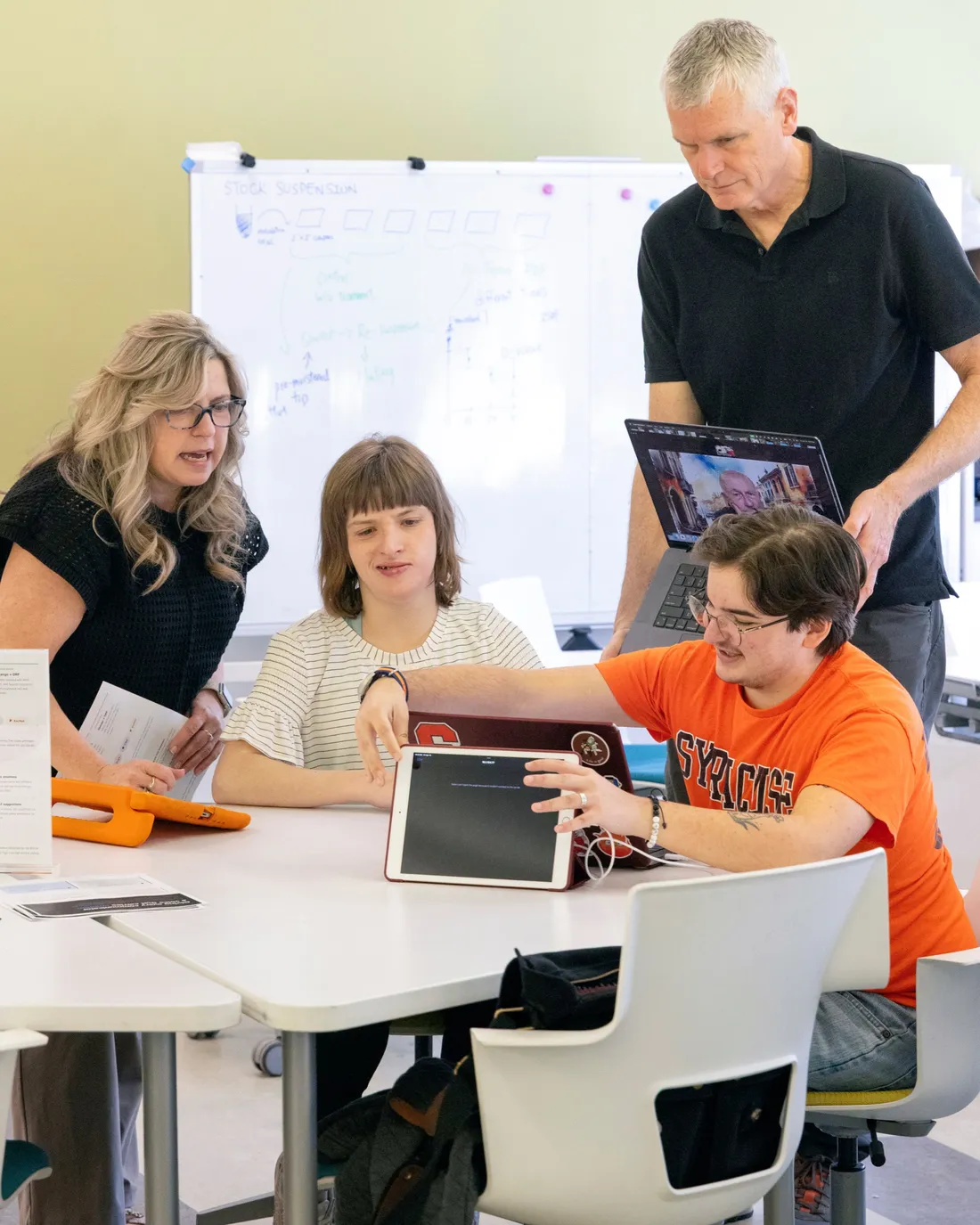Intelligence++ professor Don Carr standing and speaking with students who are working on a computer.